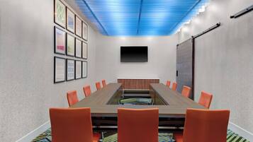 A conference room with a long table, orange chairs, a flat-screen TV, and framed pictures on the walls.