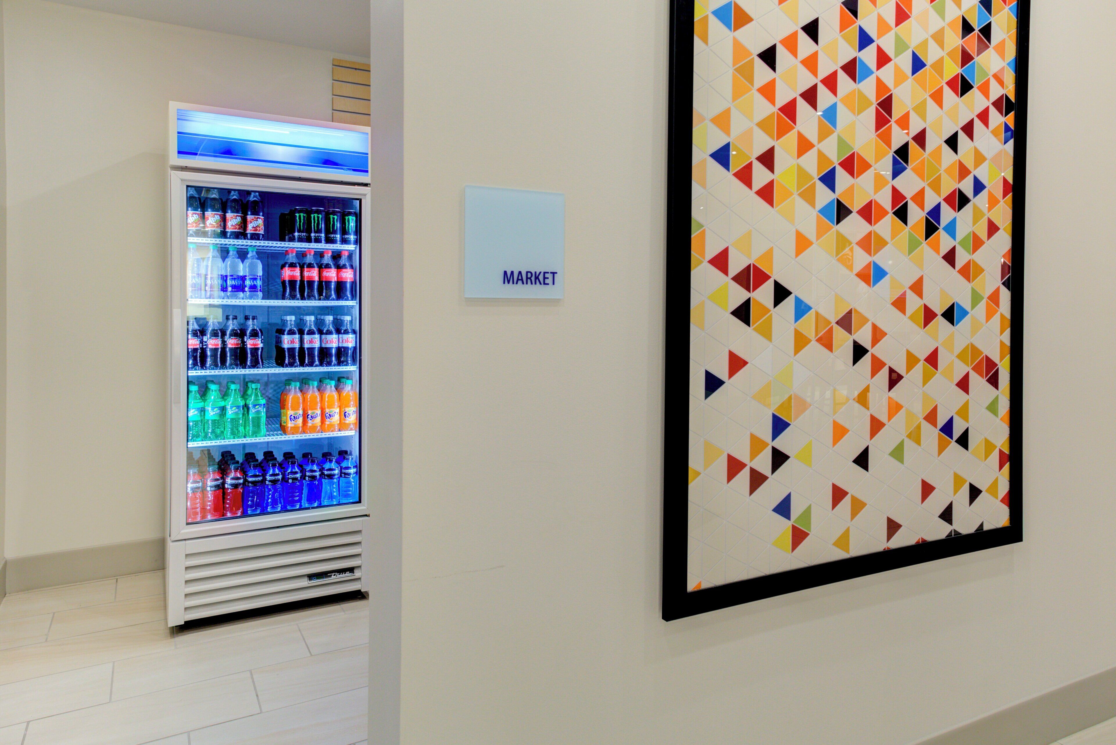 A vending machine with various beverages and a colorful geometric wall art piece.