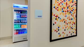 A vending machine with various beverages and a colorful geometric wall art piece.