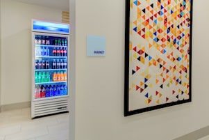 Máquina de vendas com diversas bebidas e uma vibrante obra de arte geométrica na parede.