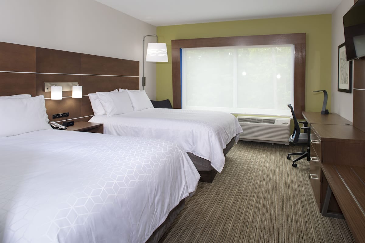 A hotel room with two beds, a desk, a chair, a lamp, and a large window.