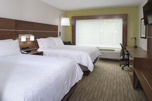 Quarto de hotel com duas camas, uma escrivaninha, uma cadeira, uma luminária e uma janela grande.
