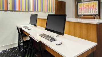 A modern office space with two desktop computers, a wooden desk, and a reception area with a colorful artwork on the wall.