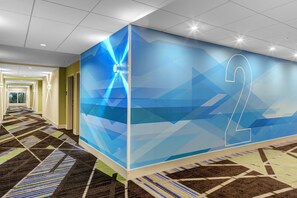 A hallway with a geometric patterned carpet, a wall with a large number '2', and a ceiling with recessed lighting. - Holiday Inn Express and Suites King George- Dahlgren by IHG (King George)