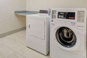 Una lavadora de carga frontal y una secadora en un cuarto de lavado con piso de baldosas.