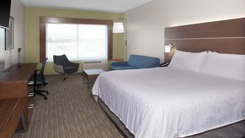 A hotel room with a large bed, a desk, a chair, a small table, and a window with a view.