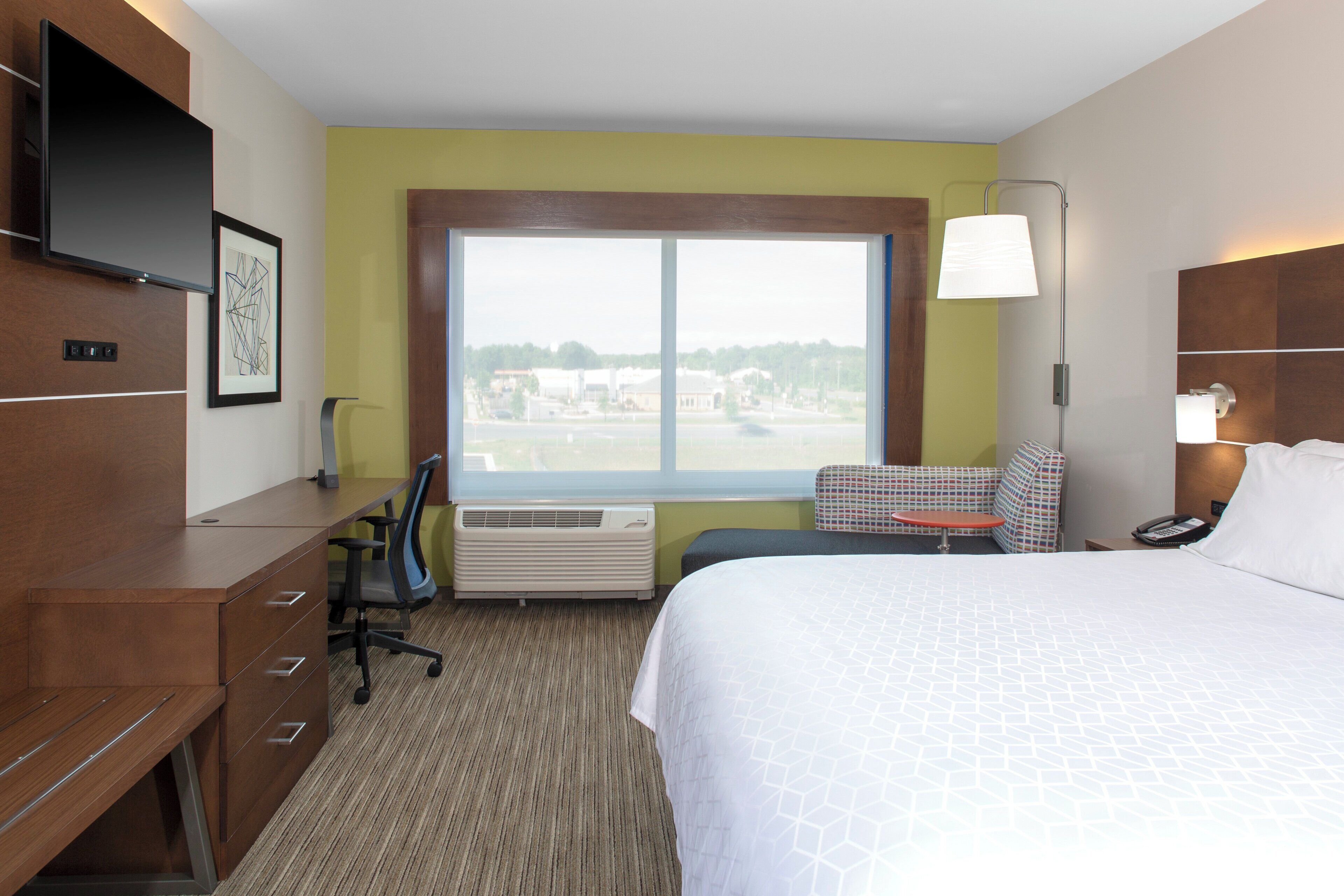 A hotel room with a bed, desk, chair, and a window with a view.