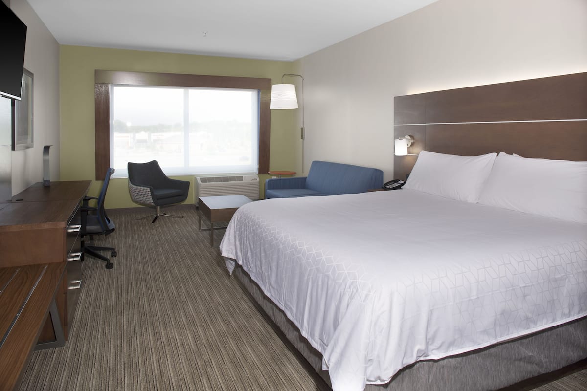 A hotel room with a large bed, a desk, a chair, and a window with a view.