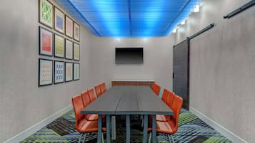 A conference room with a long table, orange chairs, framed pictures on the wall, and a blue ceiling.