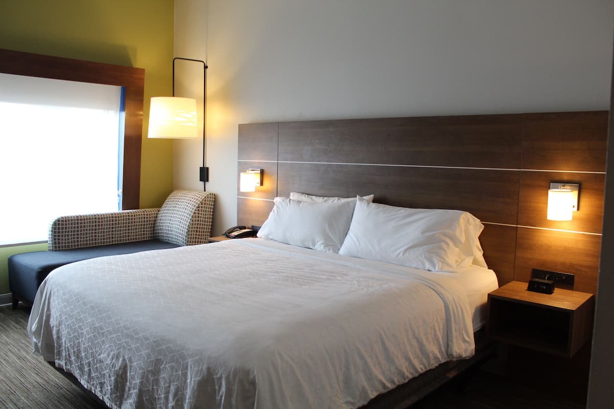 A hotel room with a large bed, bedside lamps, a nightstand, and a chair.