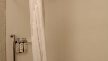 A bathroom with a white bathtub, a shower curtain, and a handrail. There are three bottles of Dove body wash on a shelf.