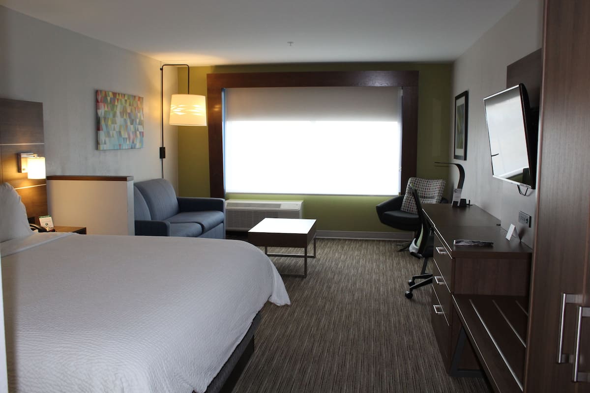 A hotel room with a large bed, a desk with a chair, a TV, and a window with blinds.