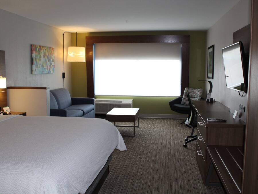 A hotel room with a large bed, a desk with a chair, a TV, and a window with blinds.