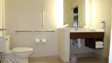 A bathroom with a toilet, a handrail, a sink, a mirror, and a trash bin.