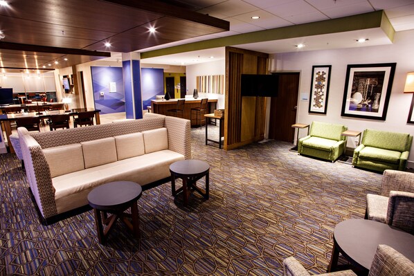 A hotel lobby with a sofa, chairs, a small table, a bar area, and a television.
