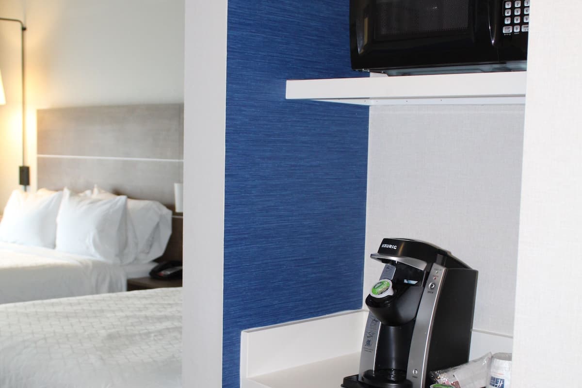 A hotel room with a bed, a microwave, a coffee machine, and a mini-fridge.