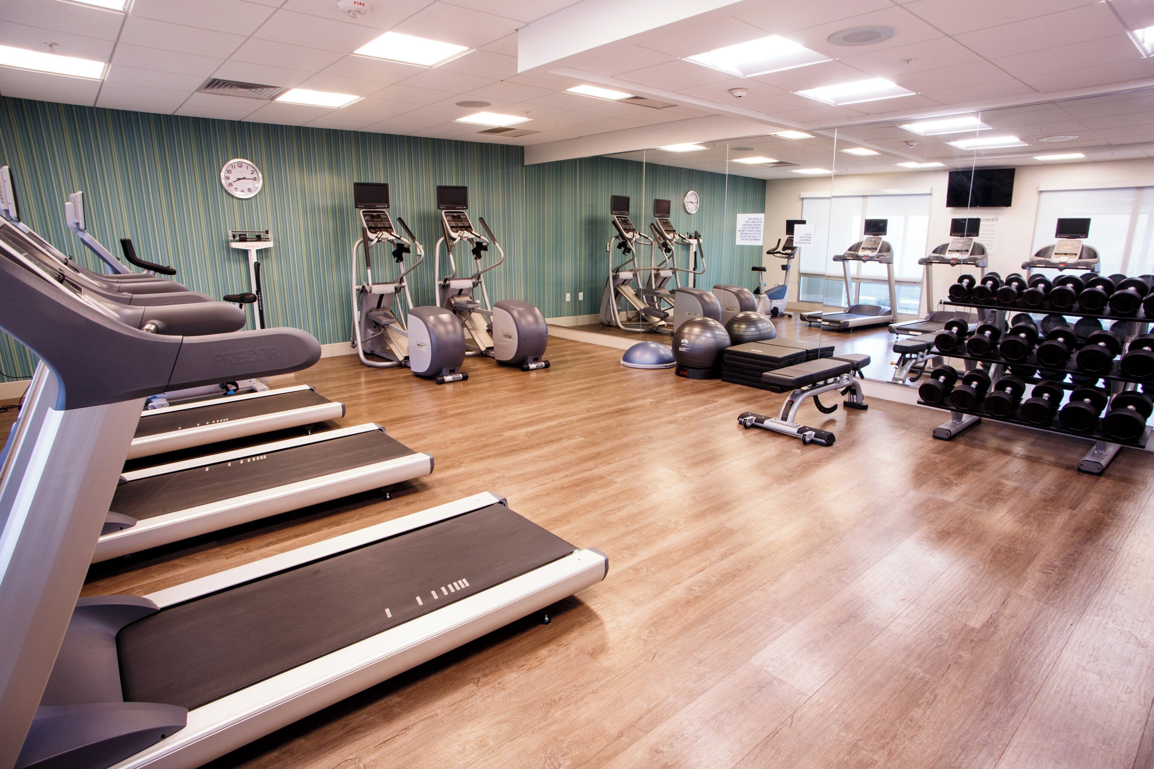 A gym with multiple treadmills, ellipticals, and a rack of dumbbells.