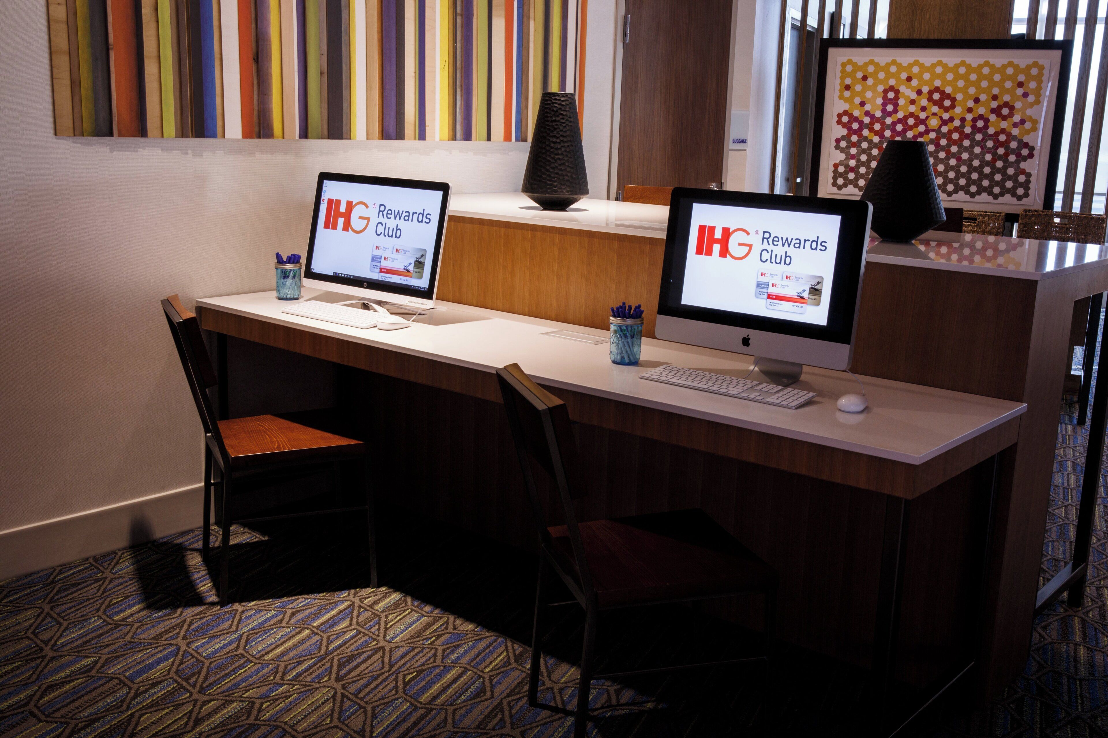 Mostrador de recepción de hotel con dos monitores mostrando el logo de 'IHG Rewards Club', un teclado, un ratón y una silla.