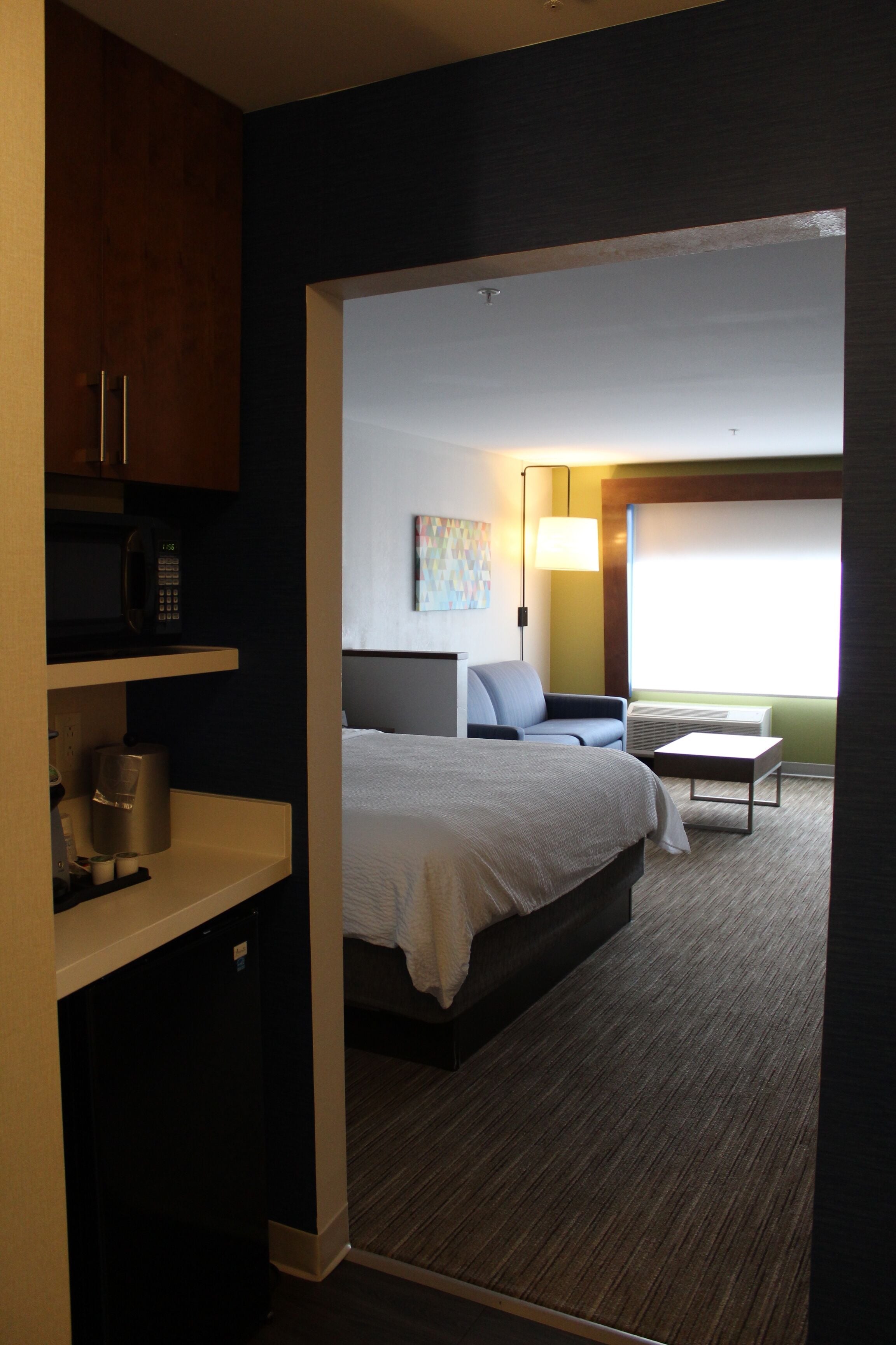 A hotel room with a bed, a desk, a chair, a microwave, and a coffee maker.