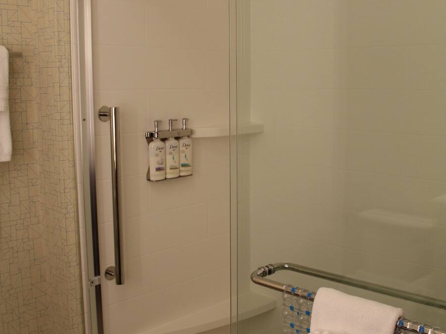 A glass-enclosed shower area with a glass shelf holding toiletries and a towel rack with a towel.
