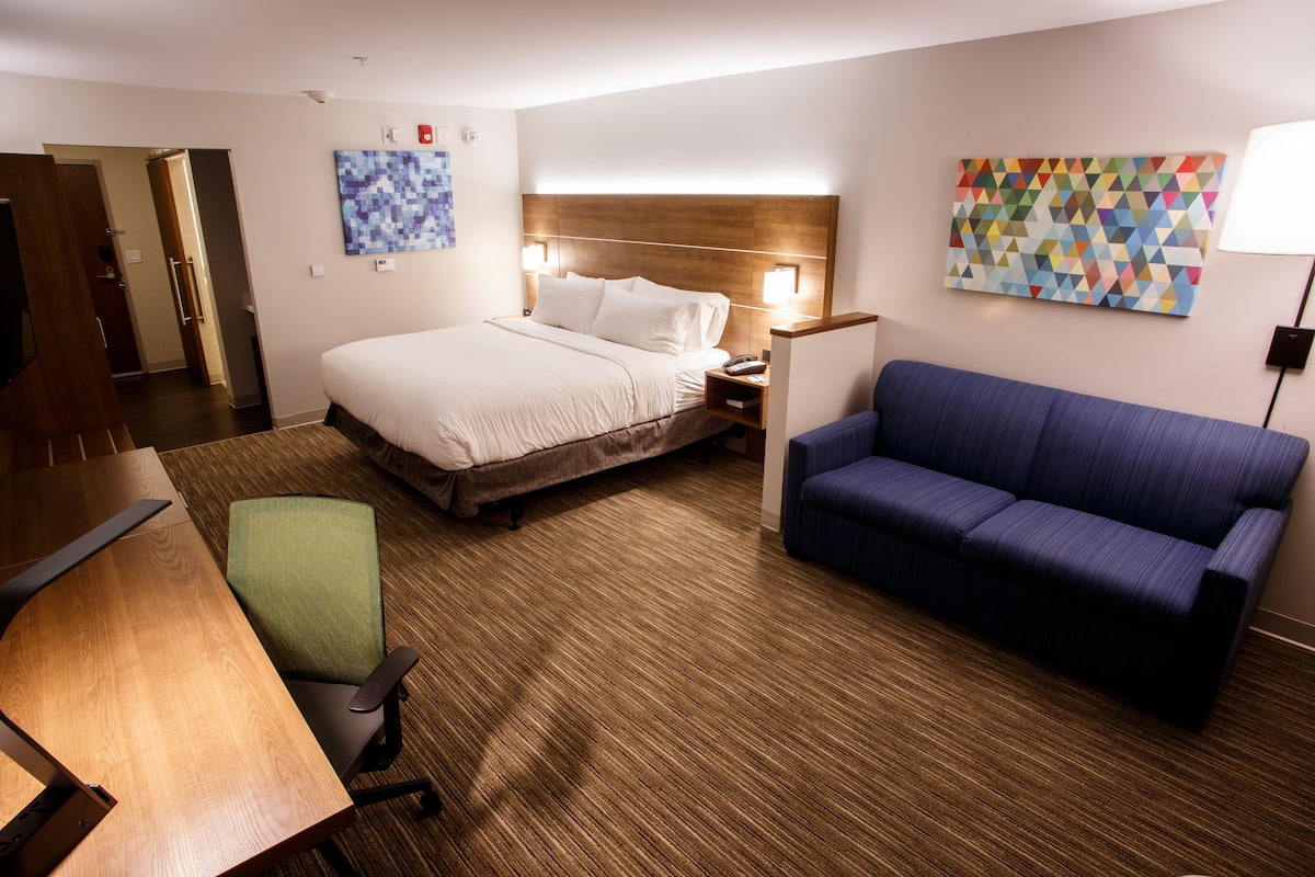 A hotel room with a bed, a blue sofa, a wooden desk, and a green chair.