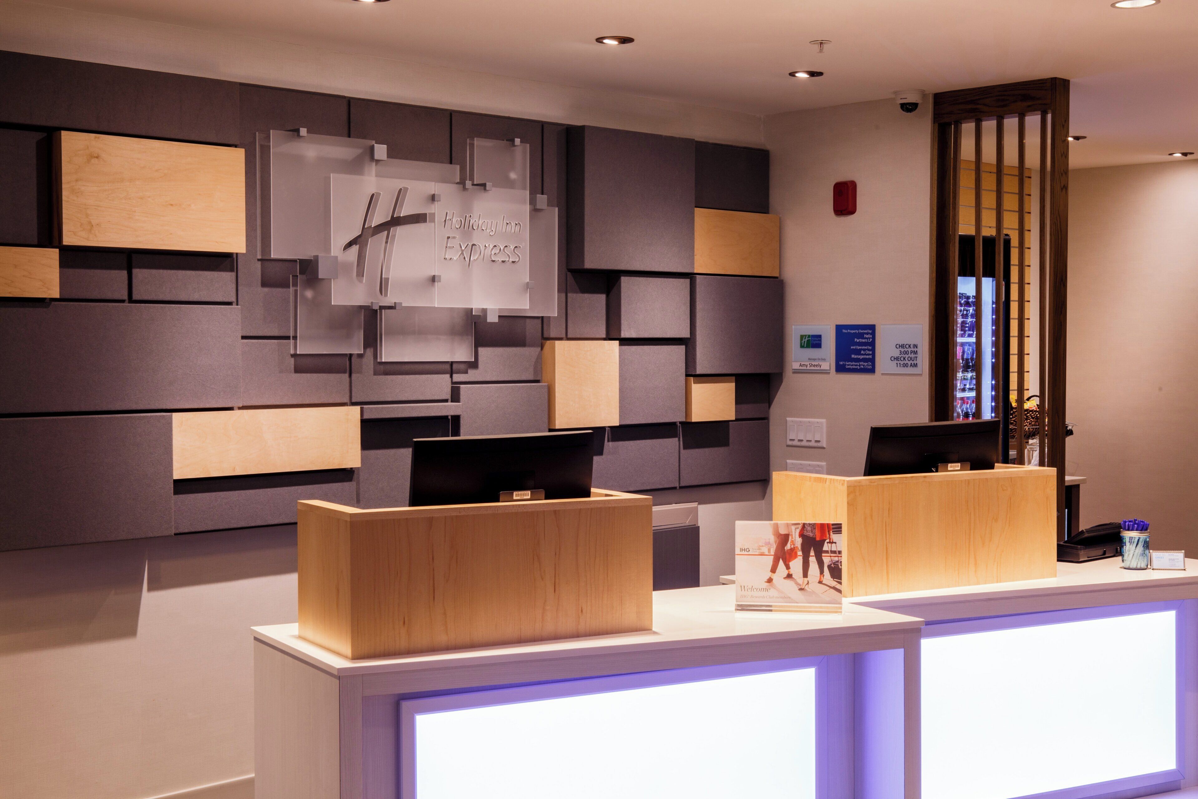 Un espace d’accueil d’hôtel au design moderne, comprenant un comptoir d’accueil, un panneau mural et une caméra de surveillance.