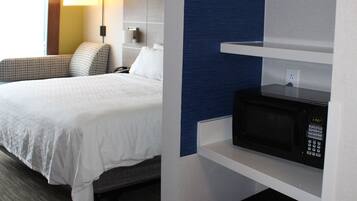 A hotel room with a bed, a nightstand, a lamp, a microwave, and a mini-fridge.