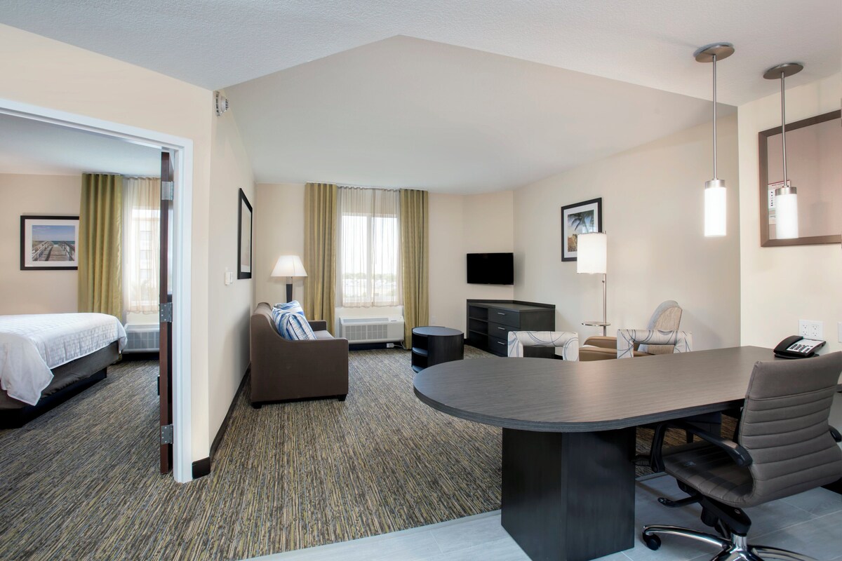 Une chambre d’hôtel avec un lit, un bureau, une chaise, une télévision et une fenêtre avec des rideaux.