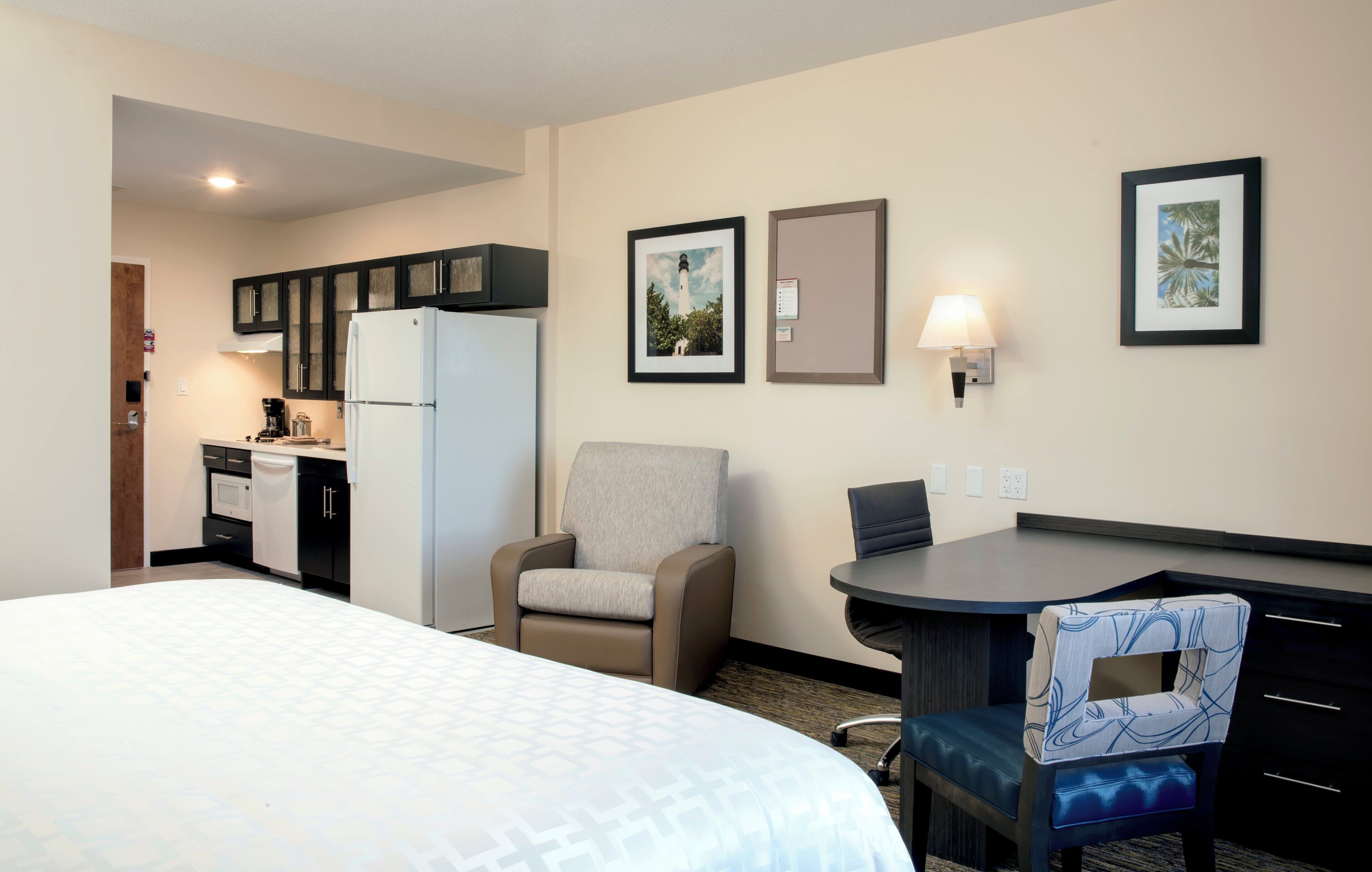 A hotel room with a bed, a desk, a chair, a refrigerator, a microwave, and a coffee maker.
