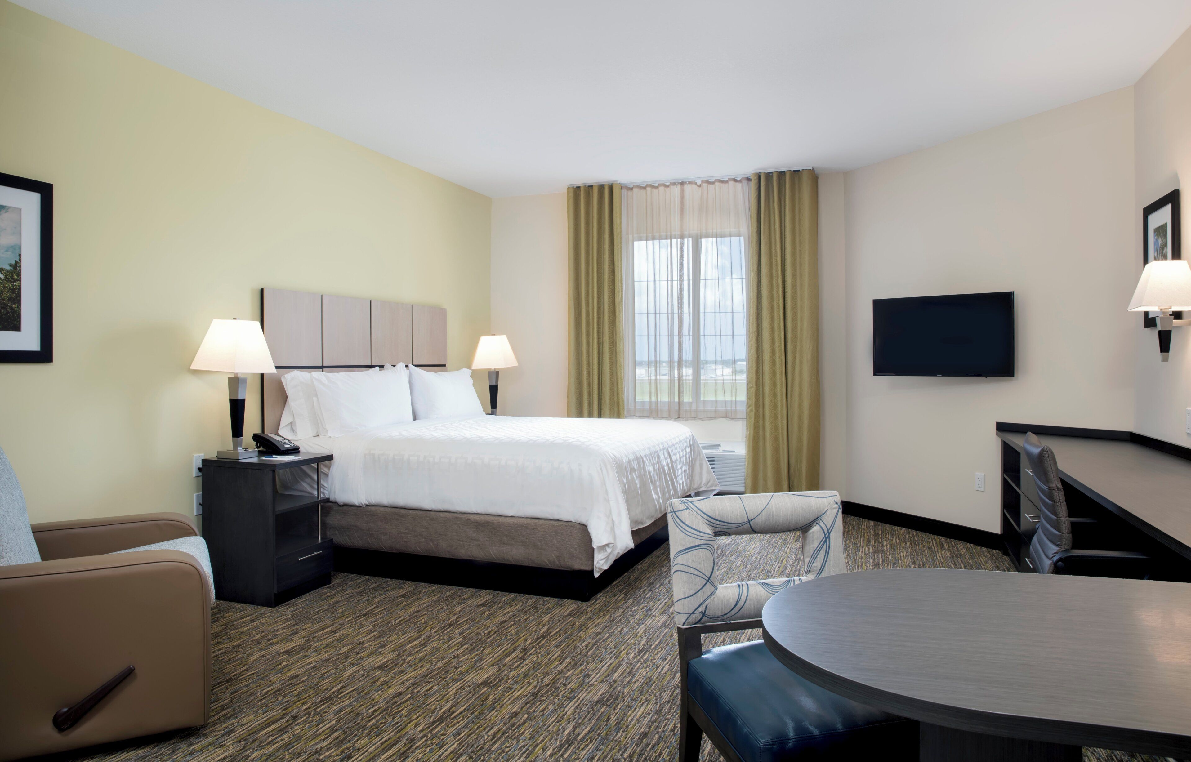 A hotel room with a bed, bedside tables, a desk with a chair, a television, and a view of the ocean.