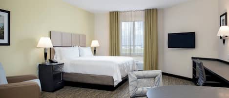 A hotel room with a bed, bedside tables, a desk with a chair, a television, and a view of the ocean.