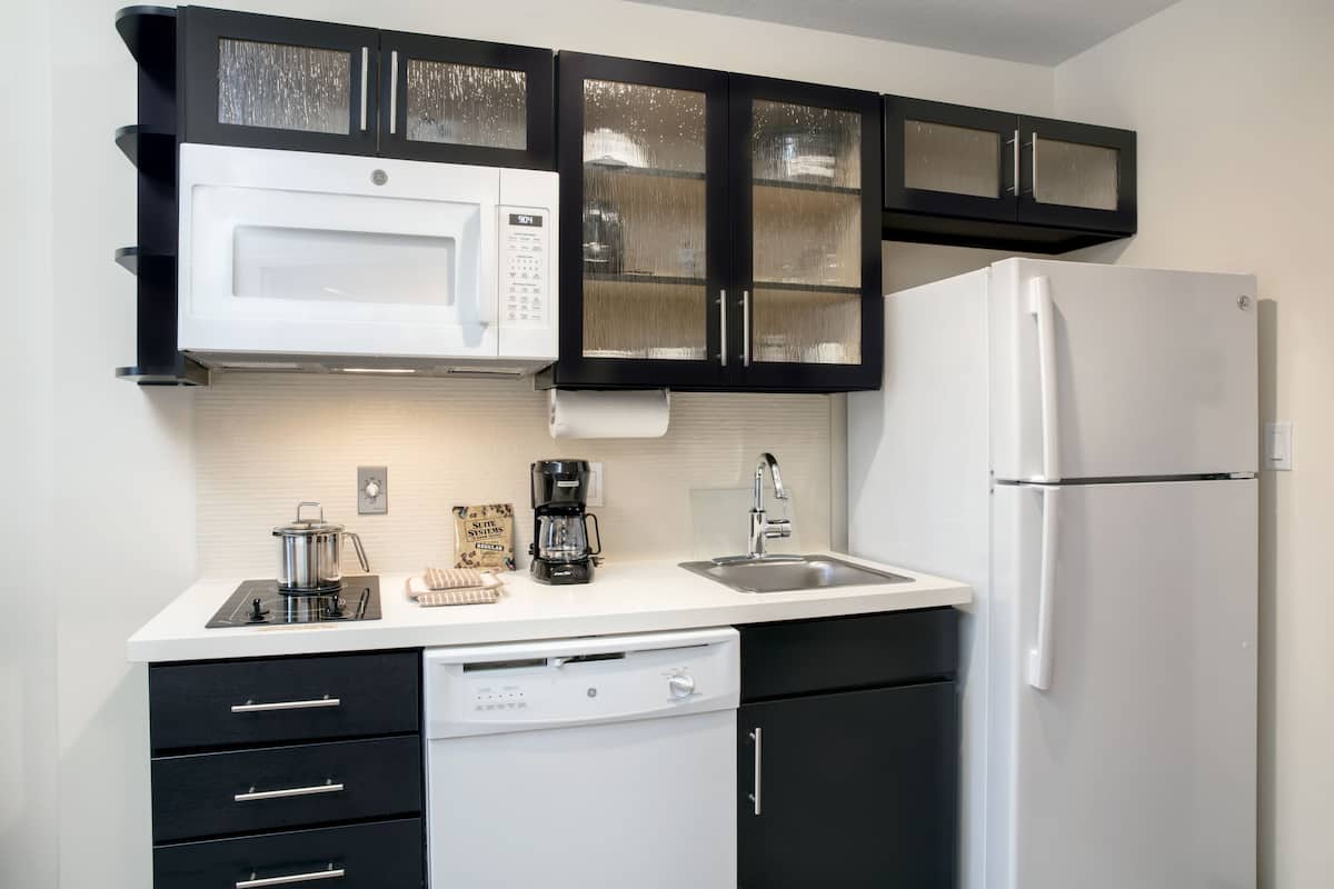 Una cocina con armarios negros, un microondas blanco, un refrigerador blanco, un lavavajillas y una cafetera.