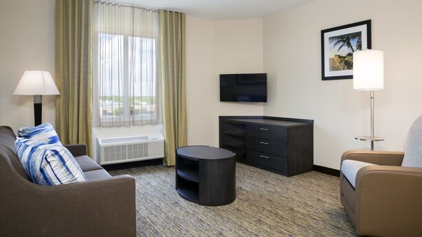 Hotelkamer met een bank, een rond tafel, een televisie, een kast en een raam met gordijnen.