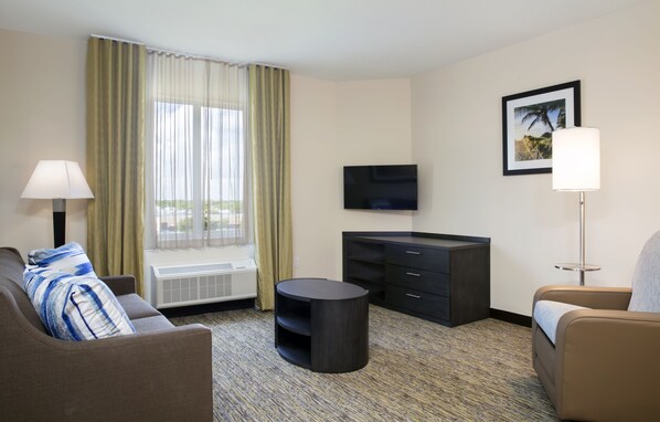 Une chambre d’hôtel avec un canapé, une table ronde, une télévision, une armoire et une fenêtre avec des rideaux.