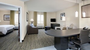 A hotel room with a bed, a sofa, a dining table, a TV, and a desk.