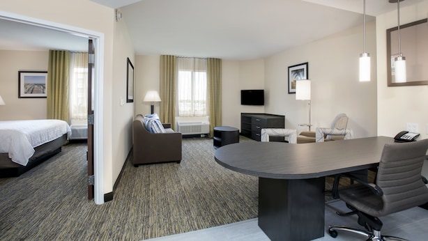 Habitación de hotel con cama, sofá, mesa de comedor, televisor y escritorio.