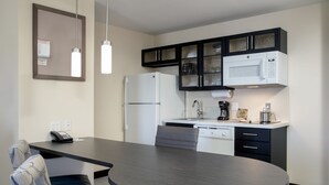 Una cocina moderna con refrigerador, microondas y cafetera. Hay una mesa de comedor con sillas y un teléfono en la pared.