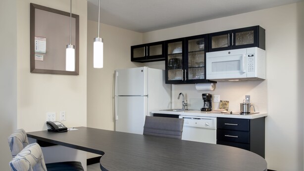 A modern kitchen with a refrigerator, microwave, and coffee maker. There is a dining table with chairs and a phone on the wall.