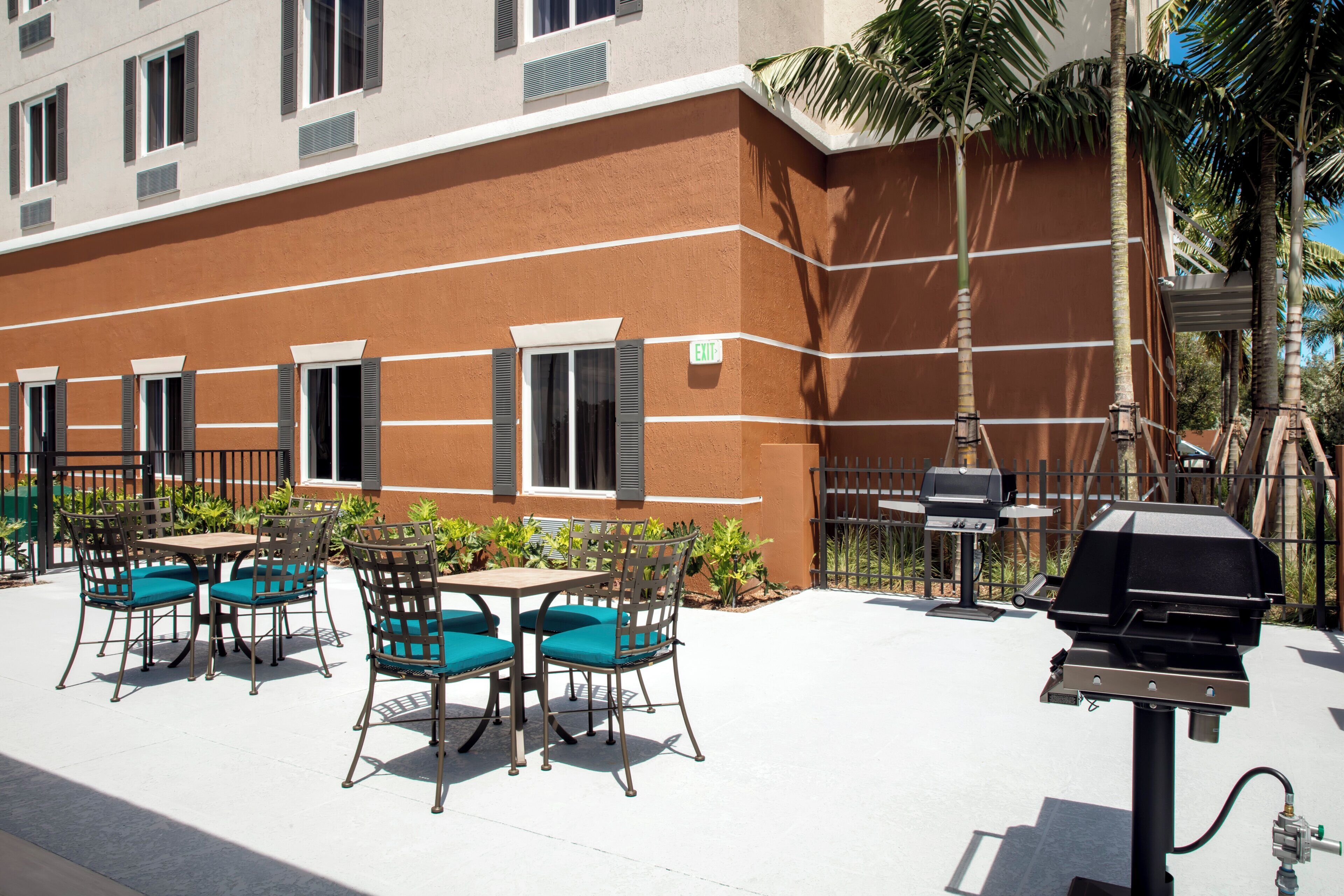 An outdoor patio with tables and chairs, a grill, and a building with windows and shutters.