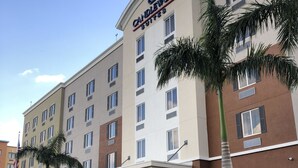 A hotel with a prominent "Candlewood Suites" sign, multiple floors, and a parking lot with palm trees.