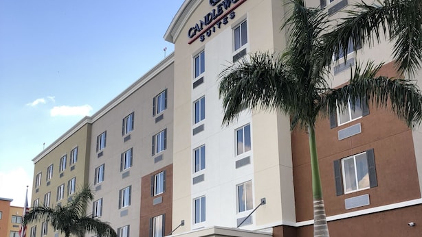 Un hotel con un llamativo letrero de "Candlewood Suites", varios pisos y un estacionamiento con palmeras.