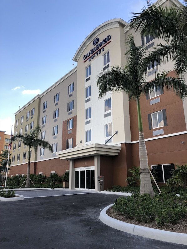 A hotel with a prominent "Candlewood Suites" sign, multiple floors, and a parking lot with palm trees.