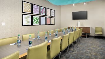 A conference room with a long table, chairs, water bottles, and framed artwork on the wall.