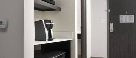 A hotel room with a microwave, coffee maker, and a refrigerator on the counter.