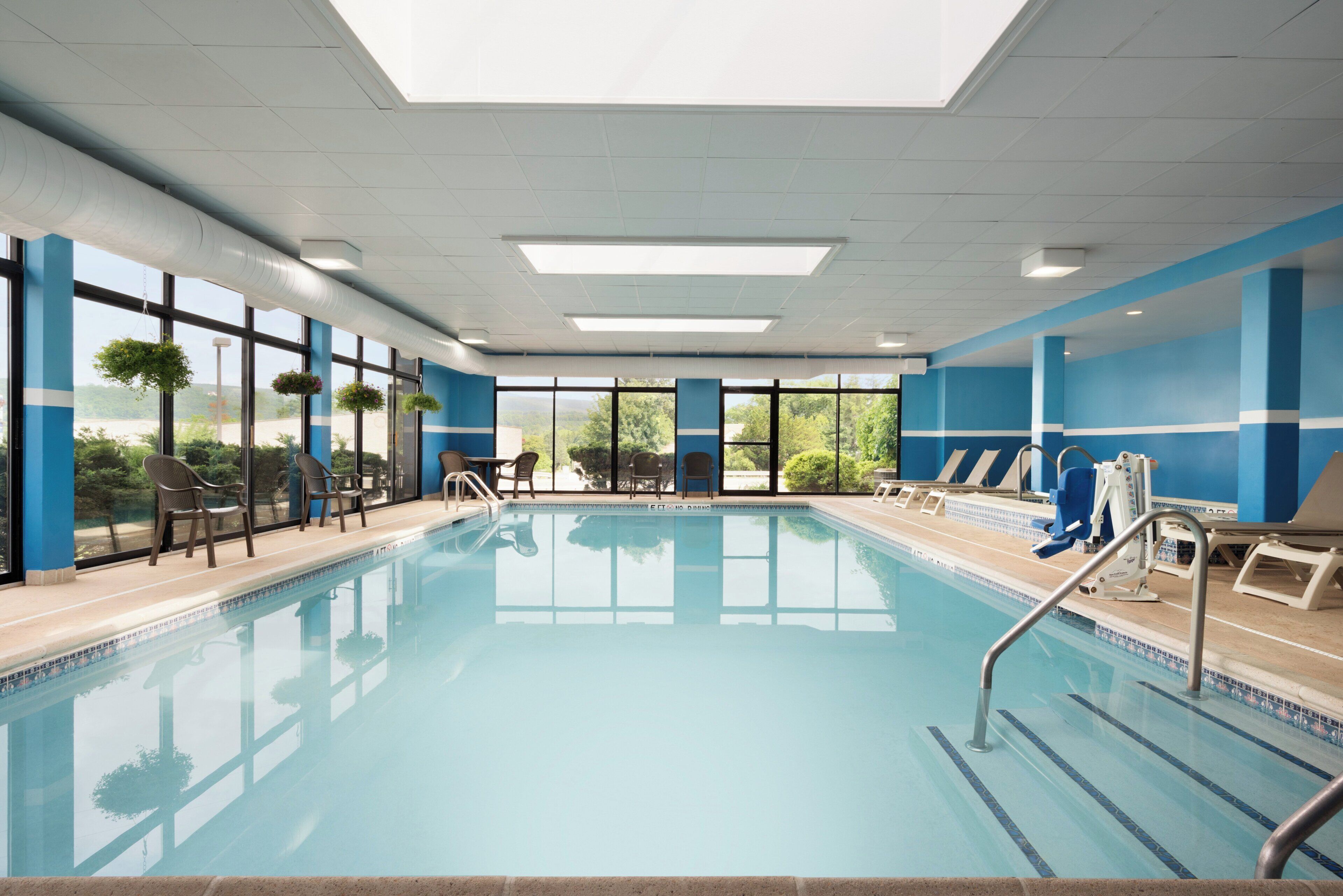 Una piscina interior con paredes de vidrio transparente, paredes azules y blancas, y vistas a zonas verdes al exterior.