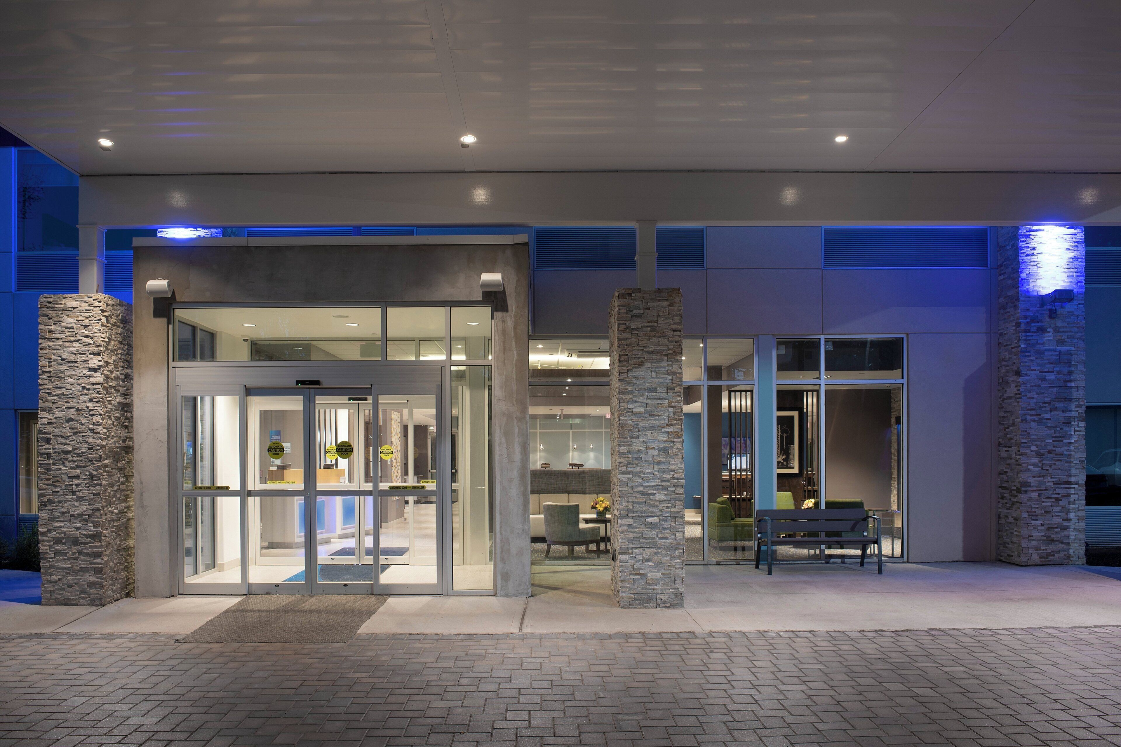 A hotel entrance with a revolving door, stone pillars, and a seating area with a bench.