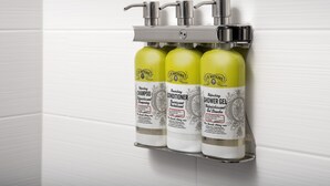 A bathroom with three bottles of J.R. Watkins products: shampoo, conditioner, and shower gel, mounted on a wall-mounted dispenser. - Holiday Inn Express and Suites North Brunswick by IHG (North Brunswick)