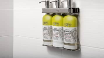 Une salle de bain avec trois flacons de produits J.R. Watkins : un shampooing, un après-shampooing et un gel douche, fixés sur un distributeur mural.