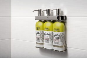 A bathroom with three bottles of J.R. Watkins products: shampoo, conditioner, and shower gel, mounted on a wall-mounted dispenser. - Holiday Inn Express and Suites North Brunswick by IHG (North Brunswick)