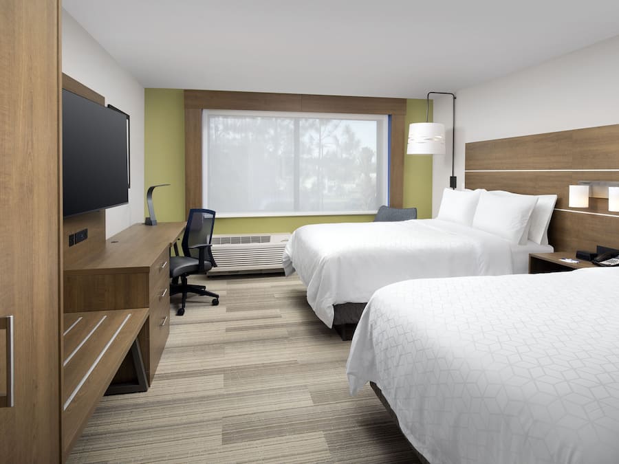 Quarto de hotel com duas camas, uma escrivaninha com cadeira, televisão e janela com vista para árvores.